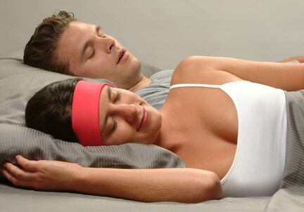man snoring in background, woman sleeping comfortably with pink SleepPhones headphones for sleeping with a snoring partner