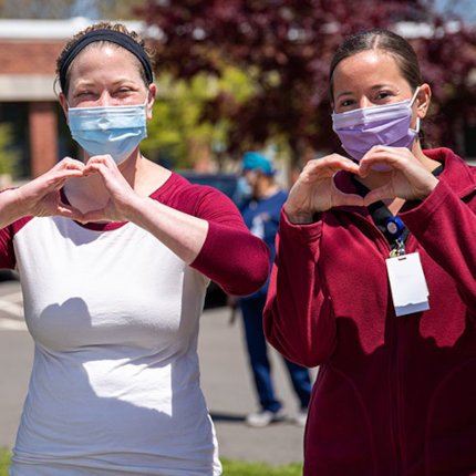 Two women with masks on making heart with hands in support of nurses with PTSD