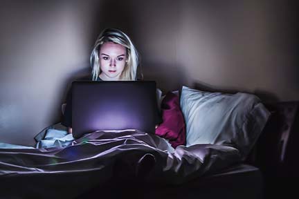 girl sitting in bed at nighttime looking at open computer